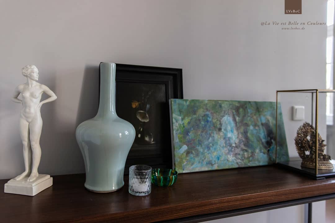 Dekoration mit Vasen und Bildern vor hellgraue Wand auf einem Sideboard